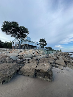 A coastal property with a large house, a rocky shoreline, and a pier extending into the water. - Waterfront Gulf 3 BR Home Ocean Springs MS - Sleeps 7 - Coastlines & Sunsets (Ocean springs)