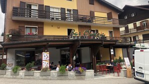 Edifici de dues plantes amb un restaurant anomenat 'Bar Olimpico' a la planta baixa. Hi ha zones d'esbarjo a l'aire lliure amb taules i cadires.