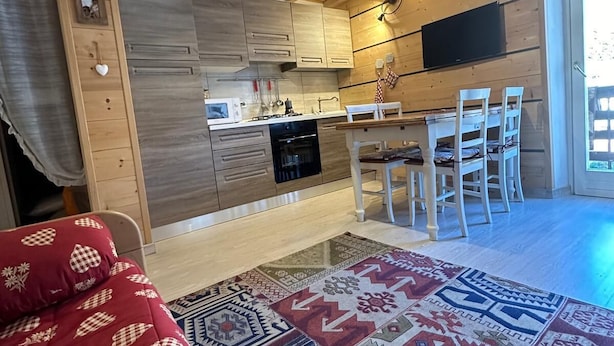 Interior de fusta acollidor amb cuina, zona de menjador i un llit amb llençol estampat.