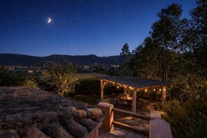 A nighttime outdoor patio area with a pergola, string lights, and a view of distant hills and a crescent moon. - Villa Bea - Piscina Privata (Cagliari)