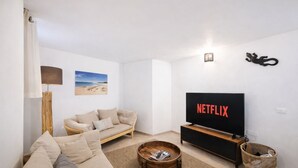 Una sala de estar con sofá, mesa de centro, televisor con el logotipo de Netflix, lámpara y una fotografía de una playa en la pared.