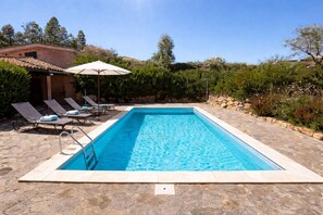 Une piscine rectangulaire bordée de pierres, entourée de chaises longues et d’un parasol.