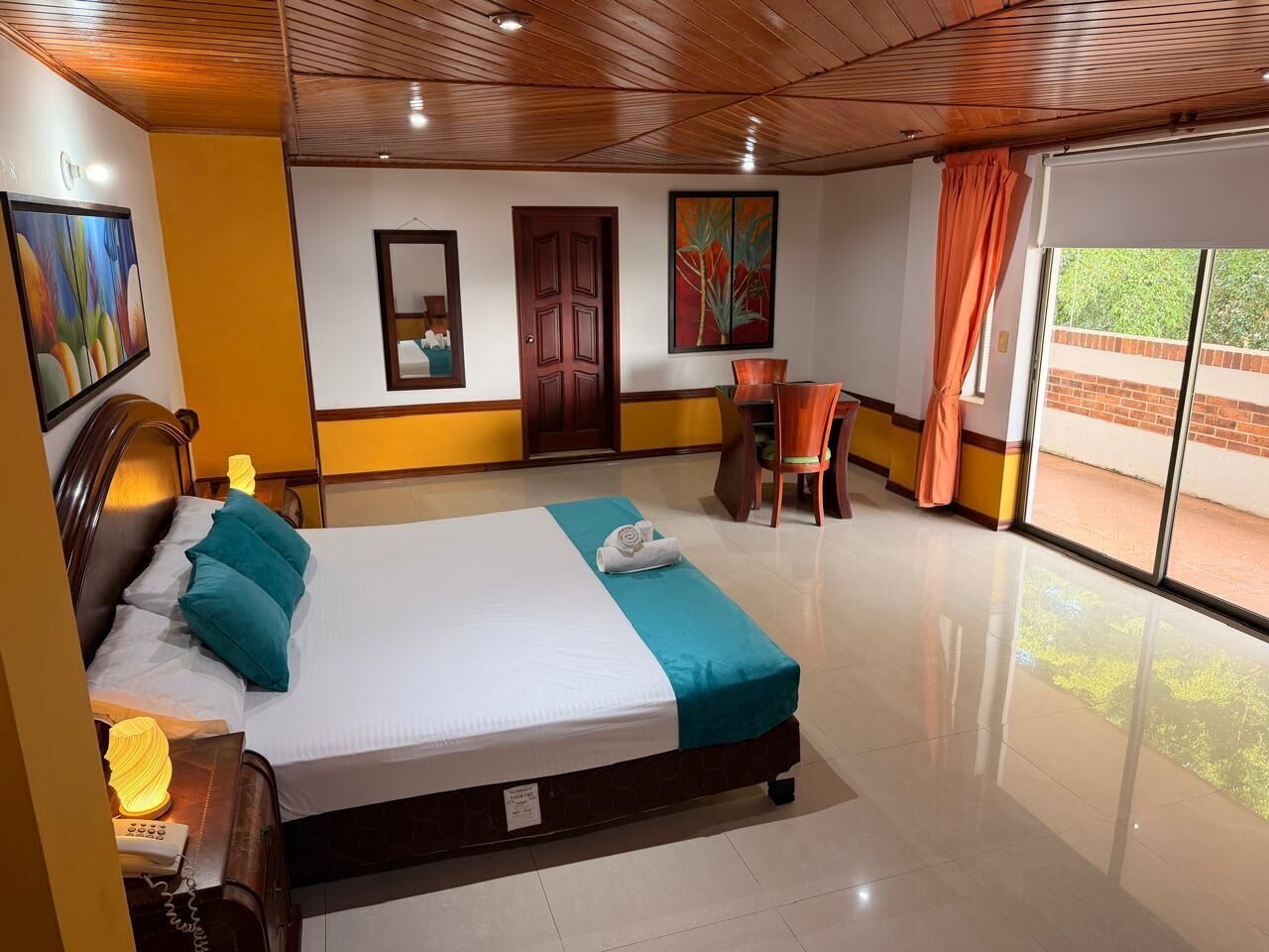 Habitación de hotel con cama, escritorio, silla, ventana y obras de arte en las paredes.