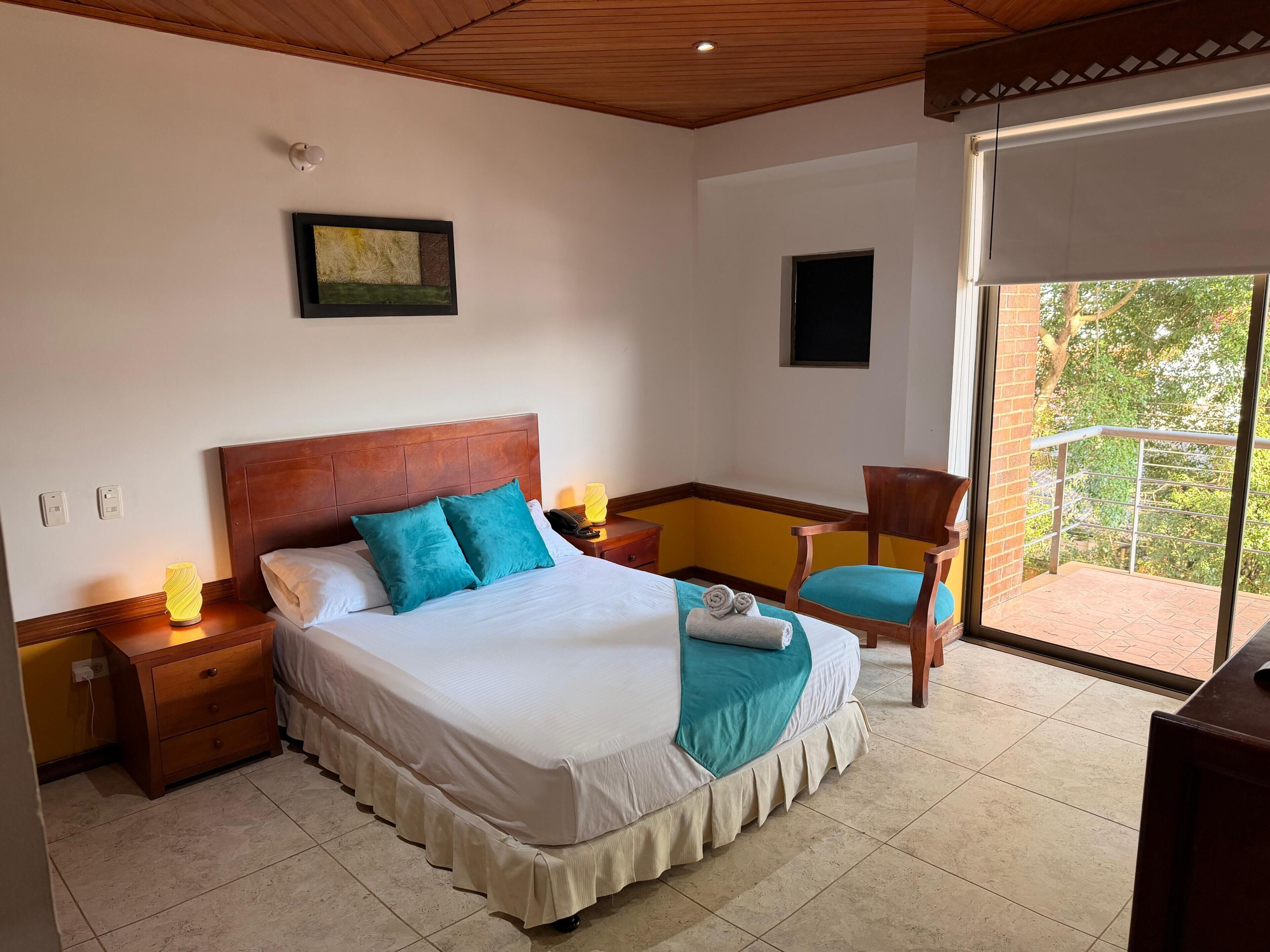 Een hotelkamer met een bed, nachtkastjes, een stoel, een balkon en een schilderij aan de muur.