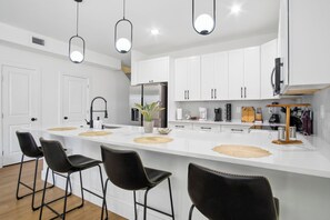 Eine moderne Küche mit weißen Schränken, einer zentralen Kochinsel mit Barhocker, Pendelleuchten und einem eingebauten Backofen.