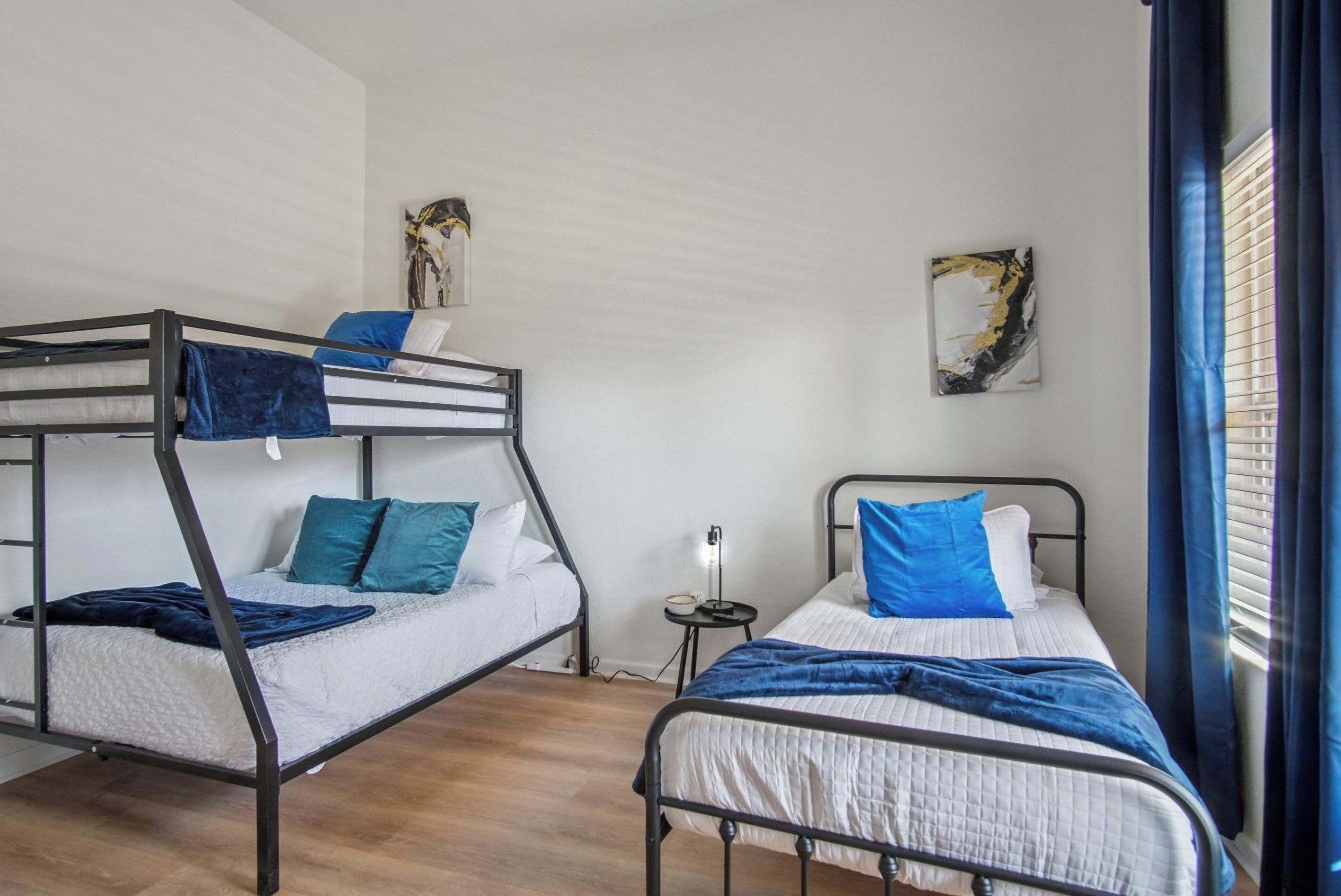 A room with bunk beds, a bedside table with a lamp, and artwork on the walls.