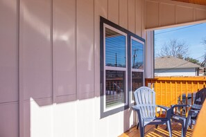 Une véranda fermée avec deux fenêtres, une terrasse en bois et deux fauteuils Adirondack.