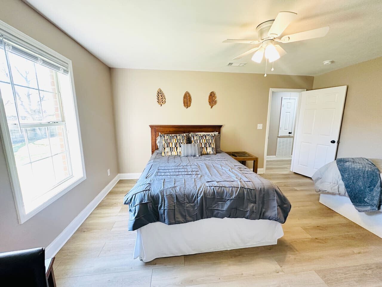 Une chambre à coucher avec un lit, un ventilateur de plafond, une fenêtre et une porte.