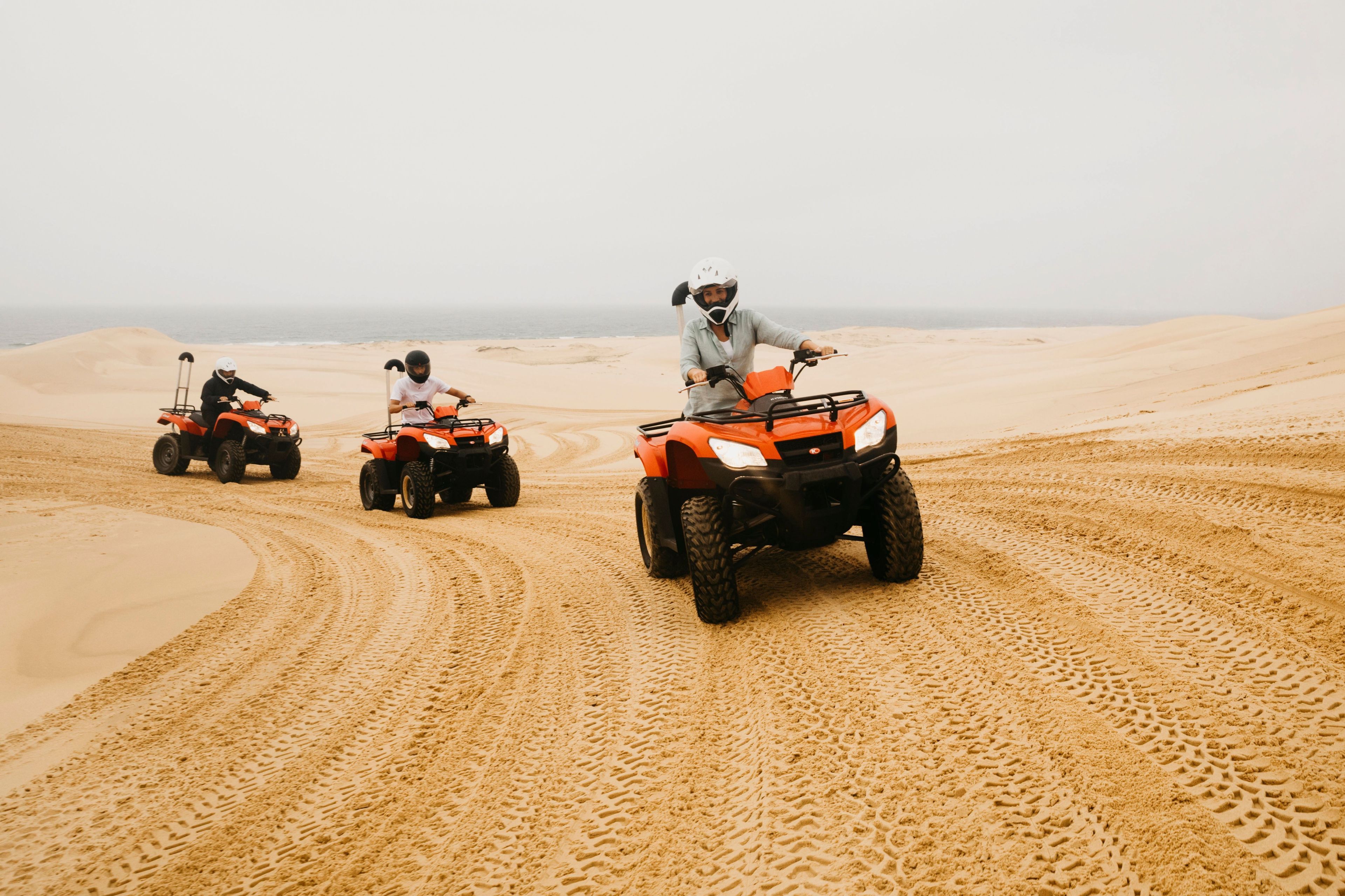 Três veículos todo-terreno em uma trilha de areia, com uma praia e oceano ao fundo.