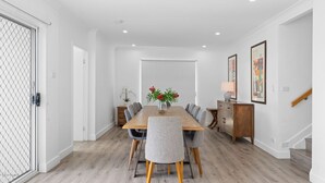 Ein Esszimmer mit einem Holztisch, grau gepolsterten Stühlen, einer Vase mit roten Blumen und einem Holzschrank.