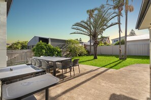 A patio area with a table and chairs, a small garden, and a white fence. - The Beachside Gathering (Anna Bay)