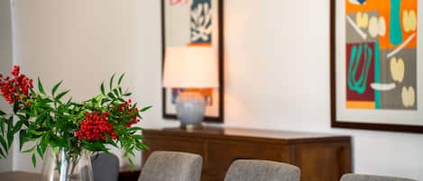 A dining table with a vase of red berries, a lamp, and framed abstract art on the wall.