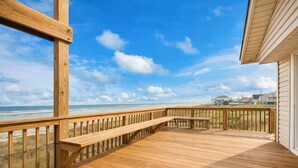 Une terrasse en bois avec un banc, donnant sur une plage et l’océan.