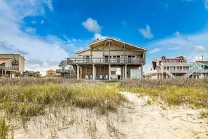 Ett hus vid stranden med en balkong, en veranda med stolar och en sandstig som leder fram till huset.