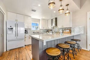 A modern kitchen with a central island, bar stools, and a refrigerator. - Beachfront-Galveston Sea Isle Best Views-Pool/Fishing Pier/Tennis Private Access (Galveston)