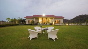 Un hotel con tejado rojo, un césped con sillas blancas y una mesa.