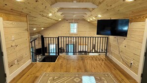 An attic room with wooden walls, a large rug, a TV, and a window. - Carvin Cottage - Cozy 2bdr with Loft- 4 Passenger Golf Cart Included (Daufuskie Island)