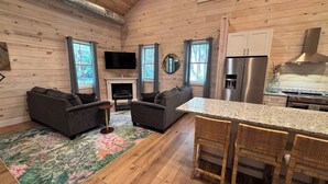 A log cabin interior with a living room, fireplace, kitchen, and dining area. - Carvin Cottage - Cozy 2bdr with Loft- 4 Passenger Golf Cart Included (Daufuskie Island)