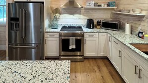 A modern kitchen with wooden walls, a stainless steel refrigerator, an oven, a microwave, and granite countertops. - Carvin Cottage - Cozy 2bdr with Loft- 4 Passenger Golf Cart Included (Daufuskie Island)