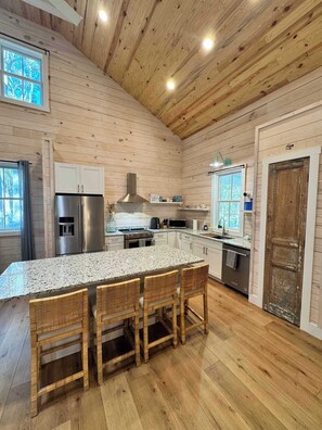 Cocina con paredes de madera, una isla de granito y un refrigerador de acero inoxidable.