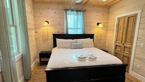 A bedroom with a wooden ceiling, a bed with white bedding, two wall-mounted lamps, and a ceiling fan. - Carvin Cottage - Cozy 2bdr with Loft- 4 Passenger Golf Cart Included (Daufuskie Island)
