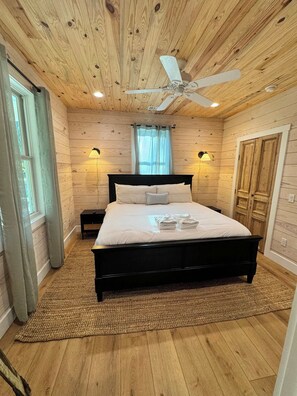 Un dormitorio con techo de madera, cama con ropa blanca, dos lámparas de pared y un ventilador de techo.
