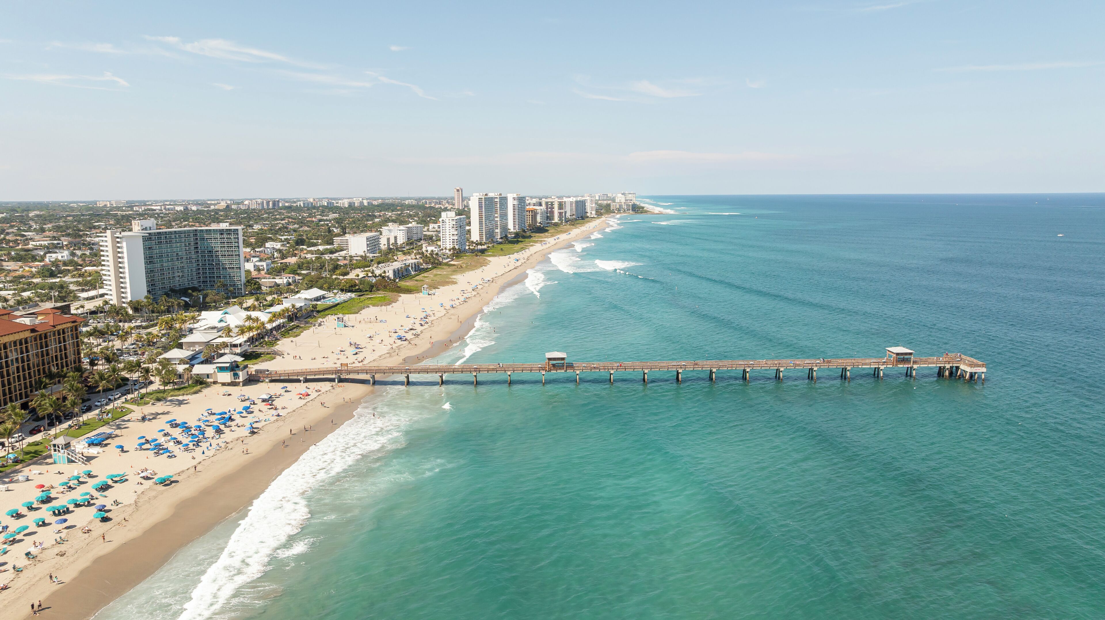A coastal cityscape with a beach, a pier, and high-rise buildings.