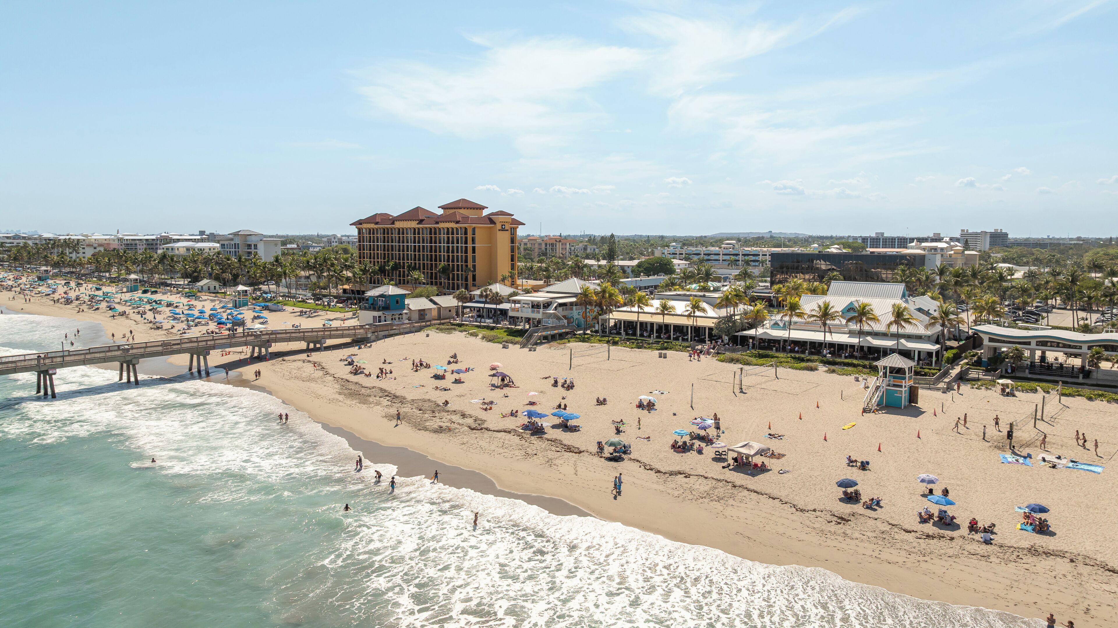 A beach with a pier, beach umbrellas, and a hotel with a distinctive roof.