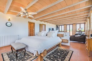 Ein geräumiges Schlafzimmer mit einem großen Bett, einer hölzernen Bank, einem Deckenventilator und Blick ins Freie.