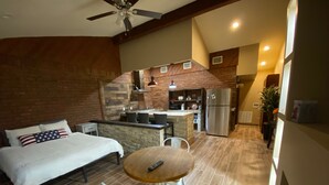 Un dormitorio con una cama, una mesa de comedor con sillas, una kitchenette y un ventilador de techo.