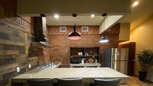 Una cocina con una isla central, taburetes de bar, un refrigerador y una planta en maceta.