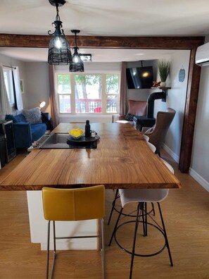 Eine Küche mit einer zentralen Kochinsel, Holzboden, einem Essbereich mit Stühlen, einer Couch und einem an der Wand befestigten Fernseher.