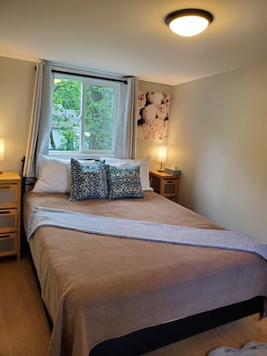 Un dormitorio con cama, dos mesitas de noche, una ventana con cortinas, una lámpara de pared y una obra de arte floral.