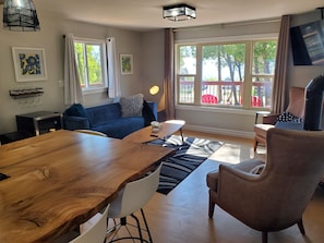 Una sala de estar moderna con una mesa de comedor de madera, un sofá azul, un sillón marrón y un ventanal con vistas al exterior.