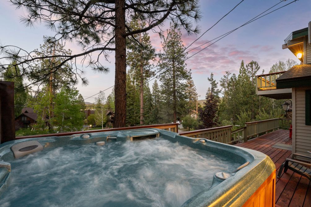 Een hottub op een houten terras, met uitzicht op bomen en een huis op de achtergrond.