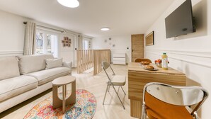 Een moderne woonkamer met een bank, een eettafel met stoelen, een aan de muur bevestigde televisie en een raam met gordijnen.