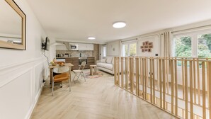 Een moderne keuken met witte kasten, een eethoek met een tafel en stoelen, en een houten leuning in een hal.