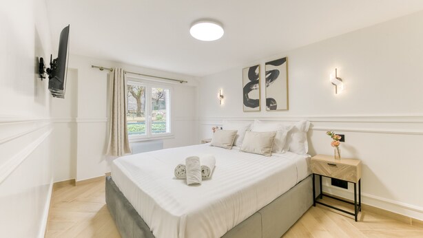 Een slaapkamer met een bed, nachtkastje, een aan de muur bevestigde televisie en kunstwerken.