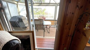 Un invernadero con puerta de cristal que da a un patio exterior con mesa, sillas y una parrilla.