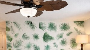 Un dormitorio con una cama grande, un ventilador de techo, una pared con diseño de hojas y una lámpara de noche.