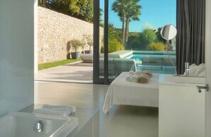 Un baño moderno con ducha envuelta en vidrio, una bañera blanca y una cama con toallas.