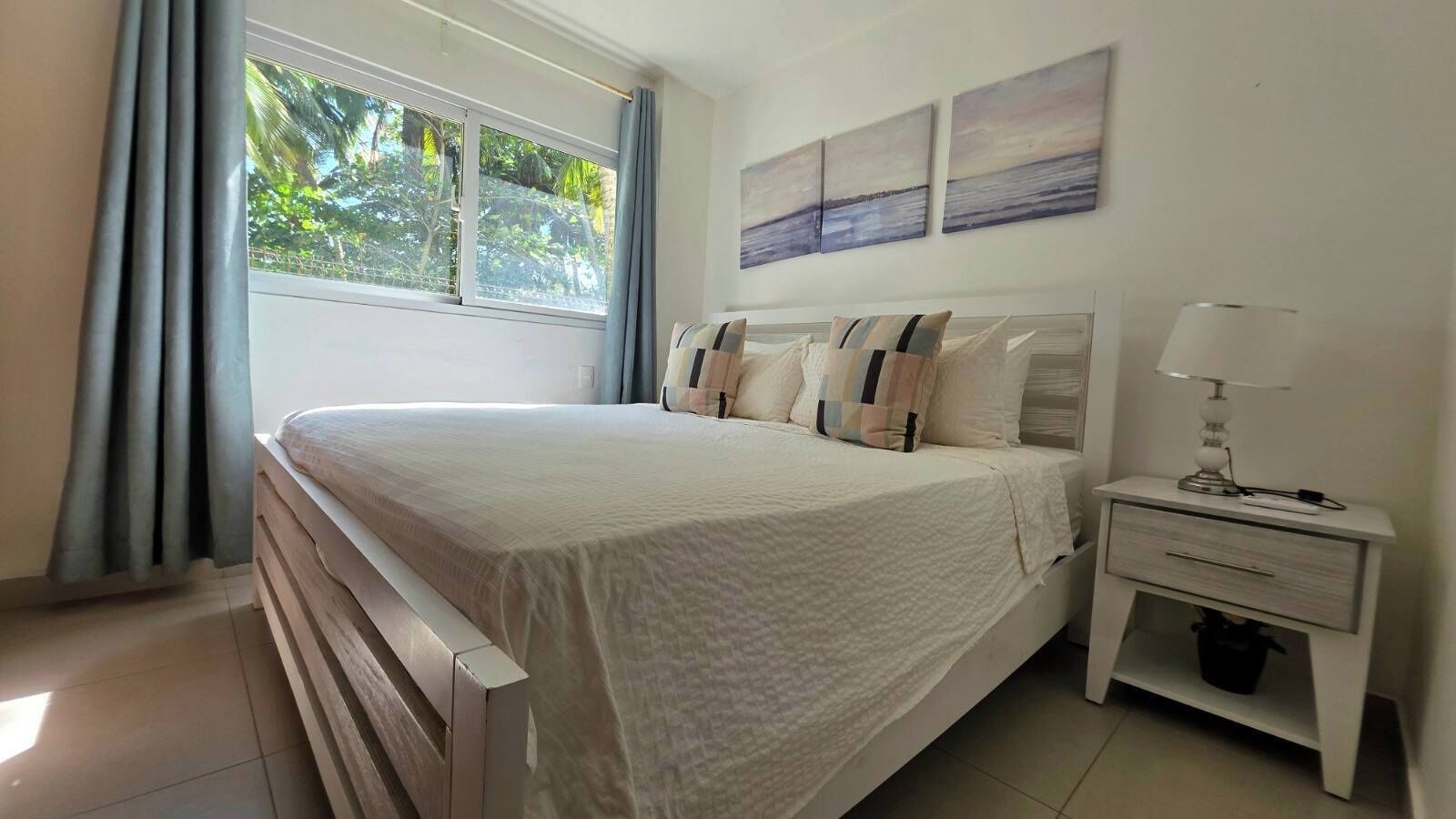 Une chambre à coucher avec un lit, une table de chevet, une lampe et une fenêtre avec des rideaux.