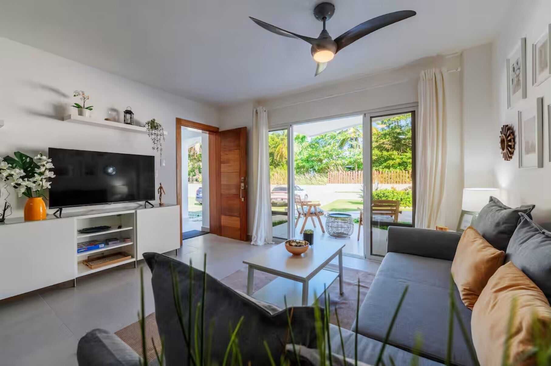 A modern living room with a flat-screen TV, a ceiling fan, a sofa, and a sliding glass door leading to a patio.