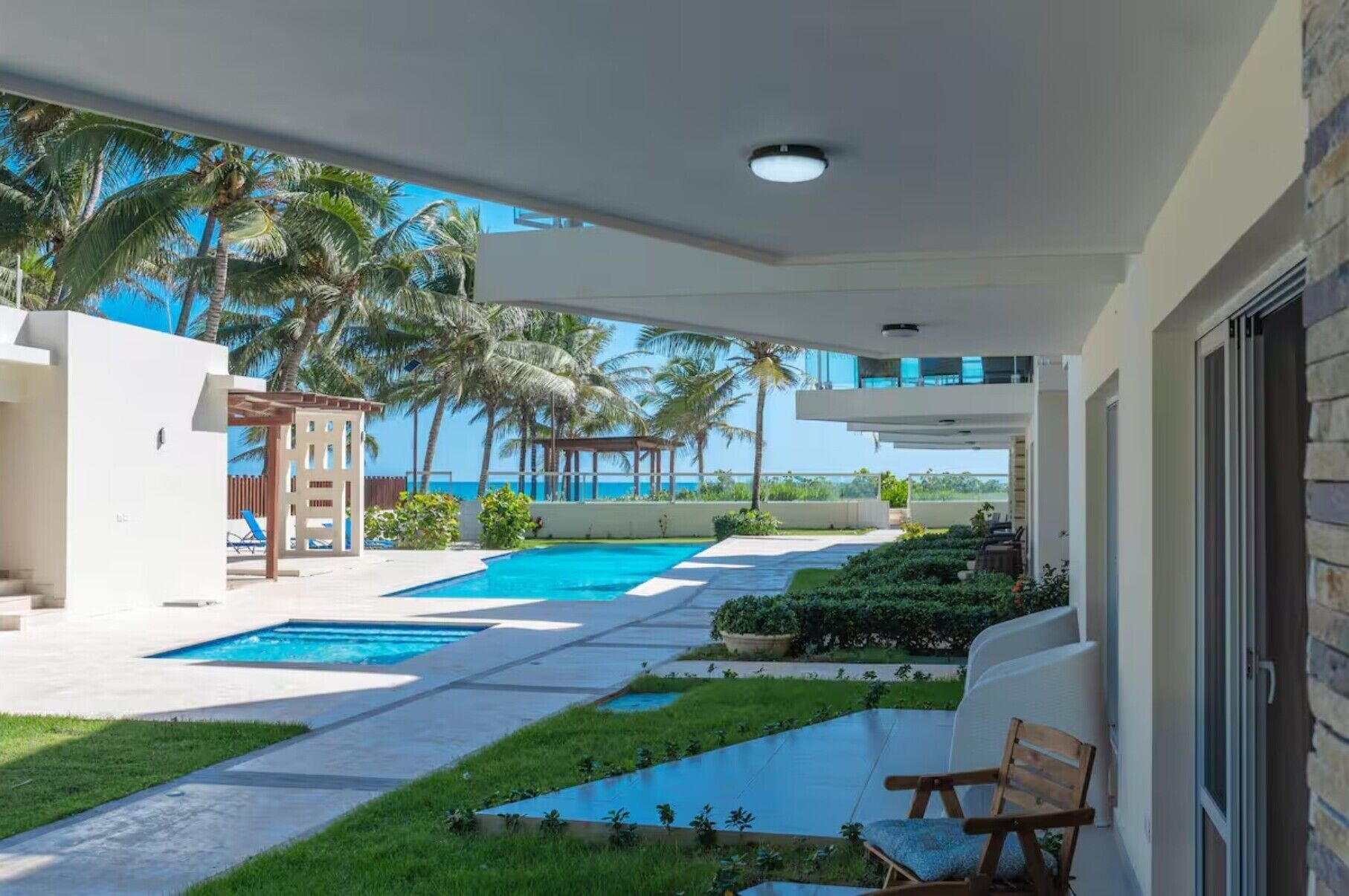 Un área de piscina con vista despejada al océano, un porche cubierto y una zona de estar con una silla.