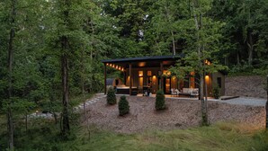 A cabin with a covered porch, outdoor seating, and a hot tub. - Cabin w/ Sauna + Hot Tub - Luxury Woods Retreat (Logan)