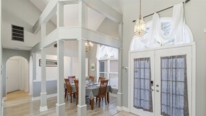 A dining area with a table set for four, a staircase, and a double door with curtains. - Hot Tub*Sauna*Pool Table*Air Hockey*King Bed*Deck (Blakeslee)