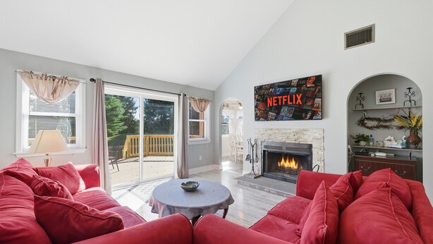 A living room with a red sofa, a fireplace, a Netflix sign, and a view through large windows. - Hot Tub*Sauna*Pool Table*Air Hockey*King Bed*Deck (Blakeslee)