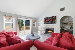 A living room with a red sofa, a fireplace, a Netflix sign, and a view through large windows. - Hot Tub*Sauna*Pool Table*Air Hockey*King Bed*Deck (Blakeslee)