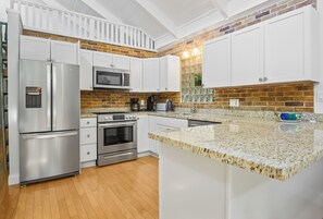 A kitchen with white cabinets, stainless steel appliances, a granite countertop, and a brick backsplash. - 2 Bedroom Island Inspired Luxury house in Downtown Islamorada (Islamorada)