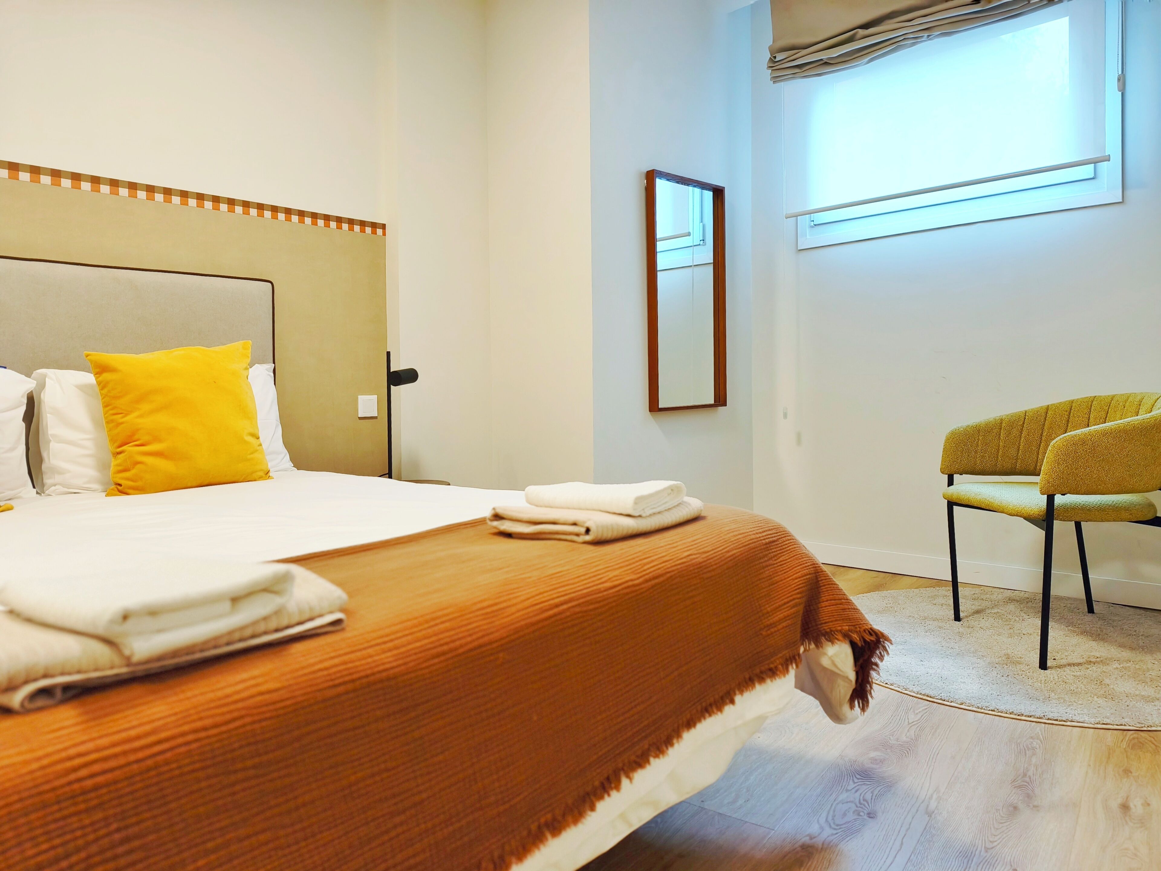 Een hotelkamer met een bed, een stoel, een raam en een spiegel.